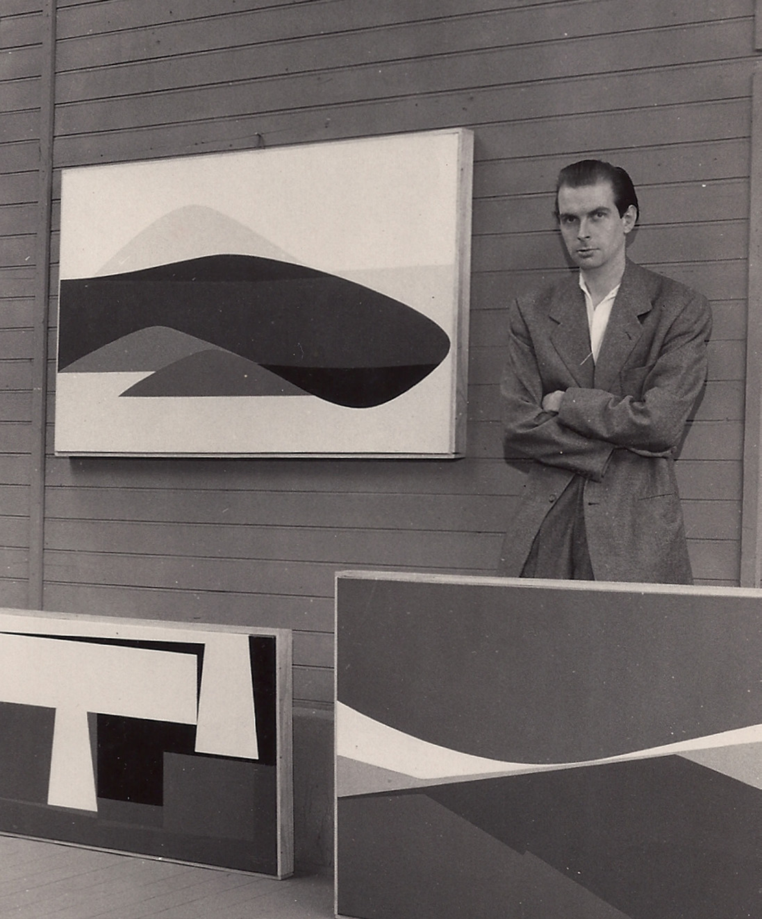 Leo Zimmerman standing with arms crossed beside his hard-edge paintings in his Paris studio