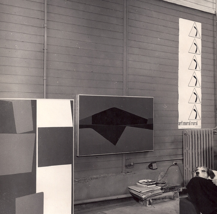 Paris studio wall with rural-mural studies and the 'art mural rural' poster, a hound dog resting at lower right